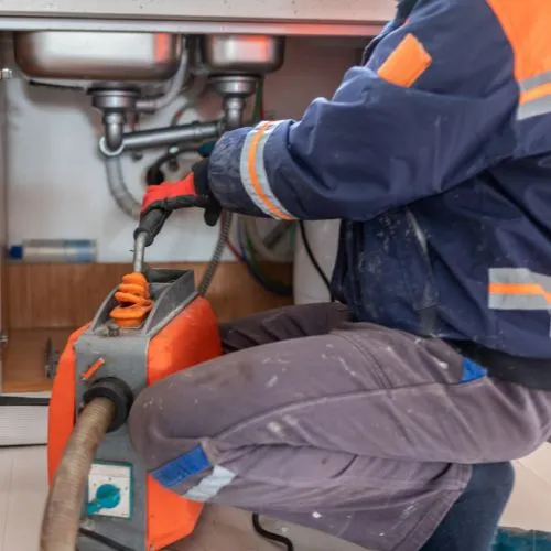 Un artisan débouche une canalisation sous un évier avec une machine de débouchage