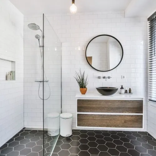 Salle de bain rénovée avec douche à l'italienne, vasque sur meuble en bois et miroir rond